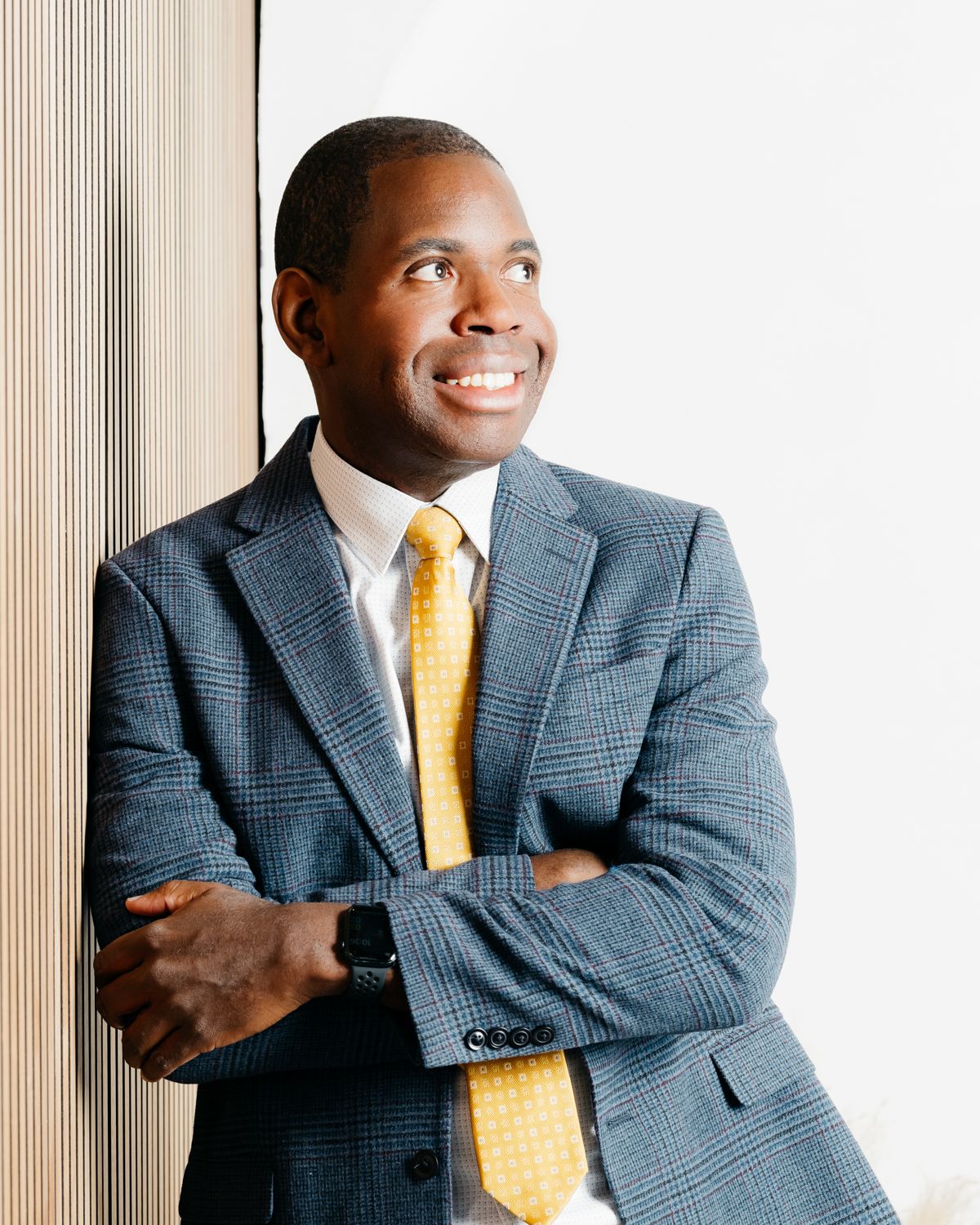 Des Dorsey leaning against a wall with arms crossed, smiling